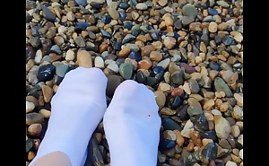 Playing with my feet in white socks with pebbles on the beach
